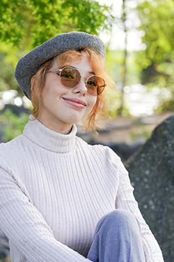 Photo of a woman with red hair wearing tinted glasses, a white sweater, and a grey beret. 